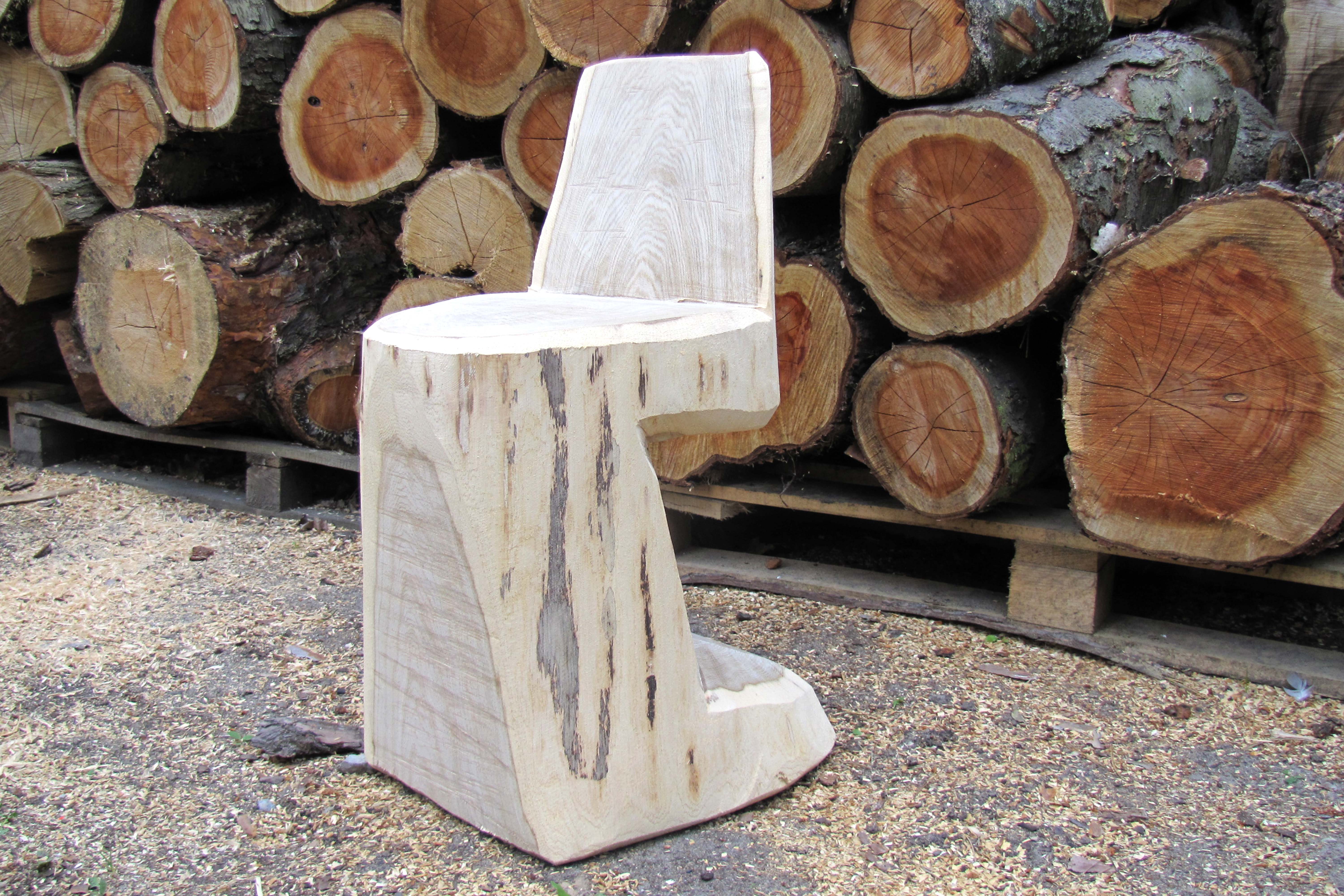 Drewniane krzesło do samodzielnego wykonania stoi przed stosem pni drzew