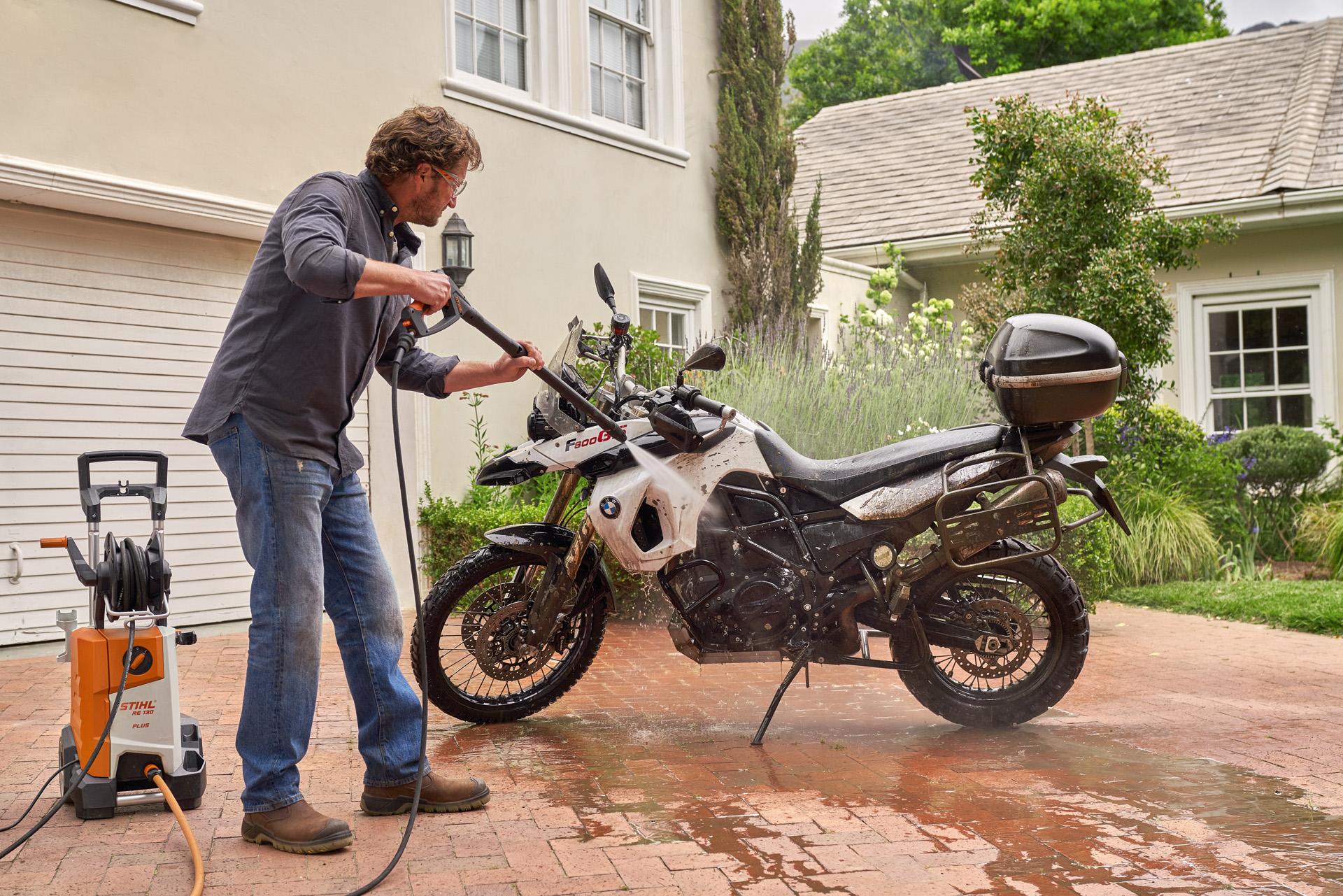 Mężczyzna czyści motocykl przed domem za pomocą myjki wysokociśnieniowej STIHL RE 130 plus