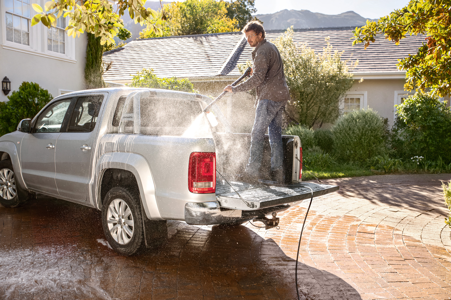 Mężczyzna stoi na powierzchni ładunkowej pick-upa i myje samochód myjką wysokociśnieniową