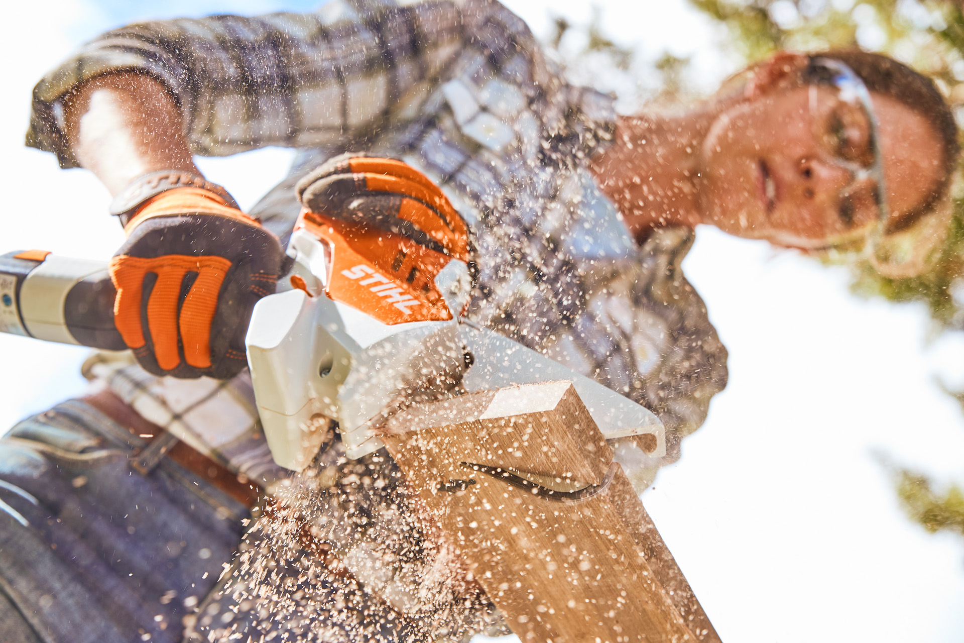 Kobieta piłująca drewnianą deskę za pomocą piły marki STIHL